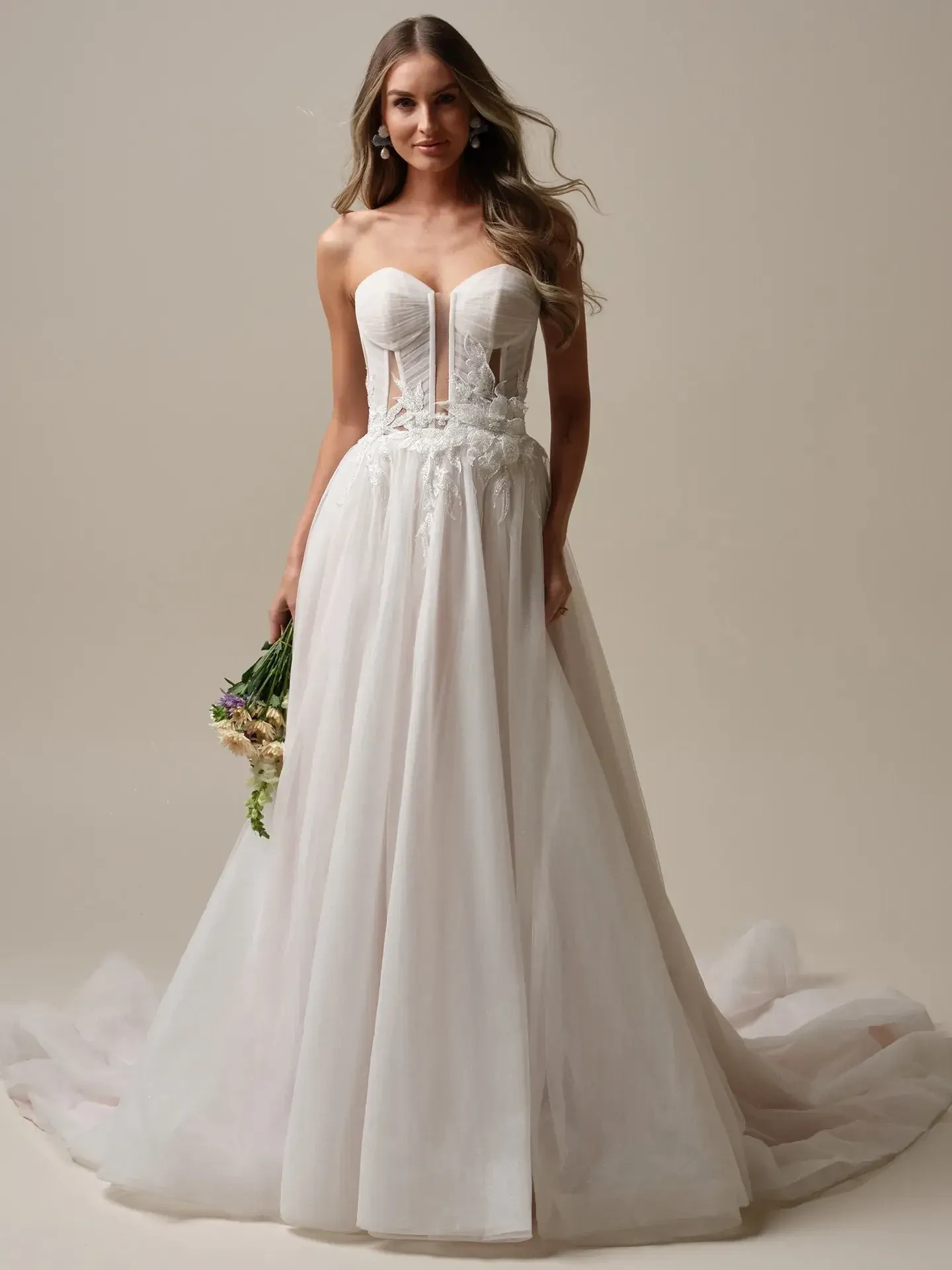 Model is wearing an a-line strapless wedding dress with a plunging neckline