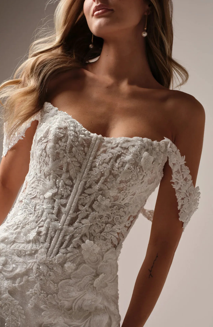 model is wearing a lace off the shoulder wedding gown