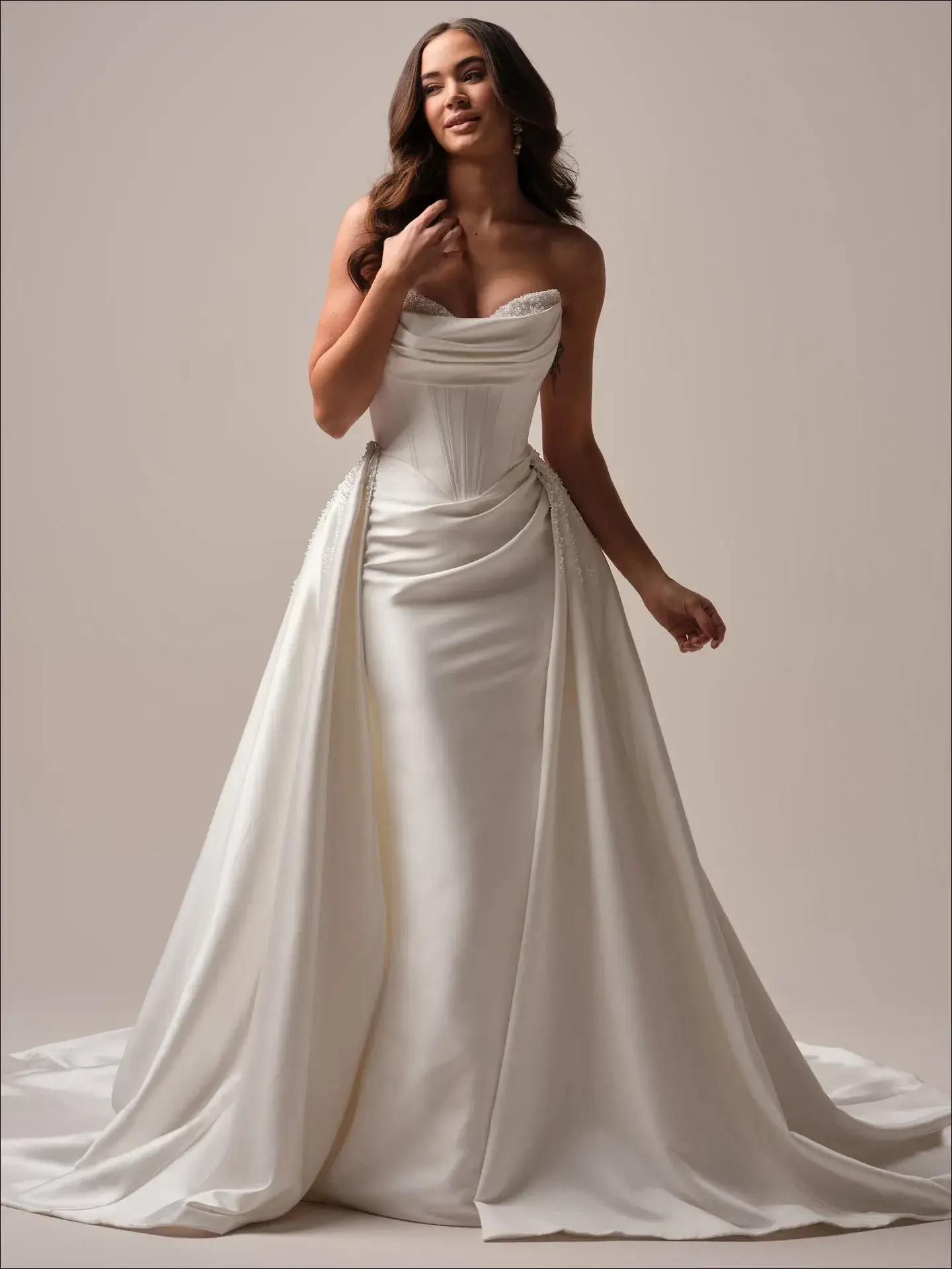 A woman wearing an elegant white gown with a fitted bodice and flowing train, standing against a neutral background.