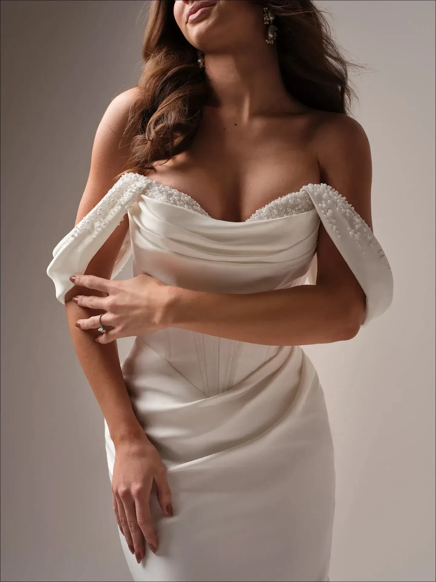 A woman wearing an elegant off-shoulder white dress with embellished sleeves, posing gracefully.